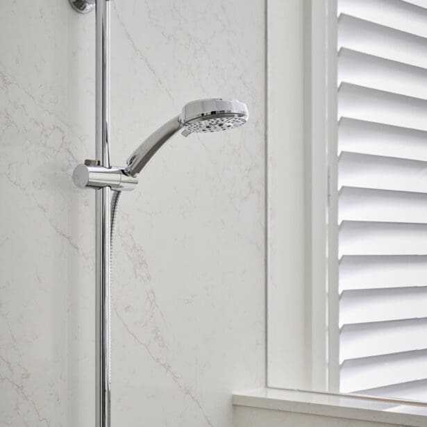 Polished chrome adjustable handheld shower mounted on marble wall with horizontal blinds in the background.