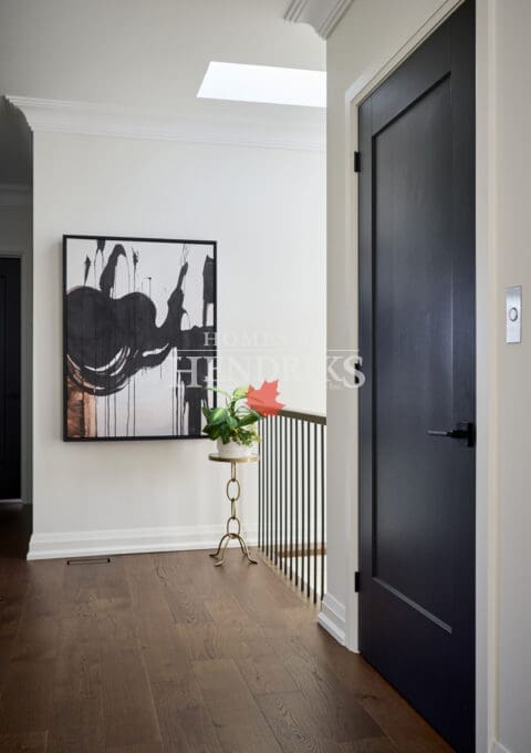 Elegant upper hallway featuring dark wood floors, matte black door, modern abstract artwork, and a skylight flooding the space with natural light.