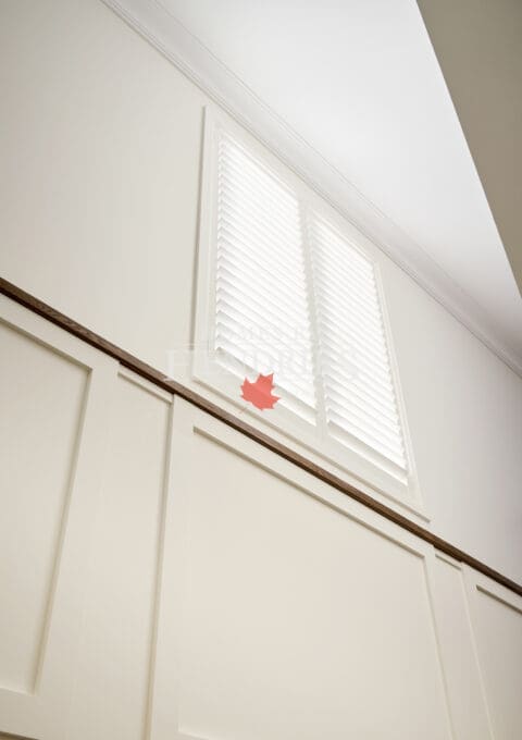 Bright upper stairwell with white wall paneling and high-set window framed by crown molding and sleek shutters.