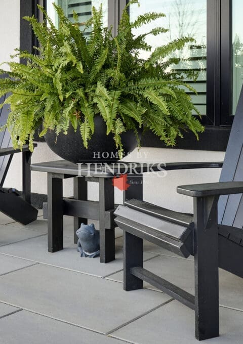 Modern front patio with black Adirondack chairs, a matching side table, and a large fern planter against a white stucco exterior.