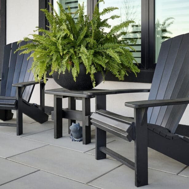Modern front patio with black Adirondack chairs, a matching side table, and a large fern planter against a white stucco exterior.