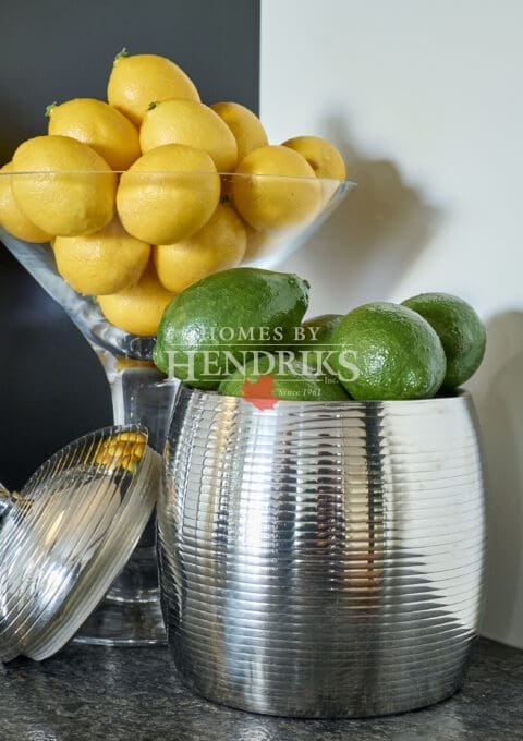 Contemporary kitchen vignette with a metallic ribbed container filled with limes beside a martini glass bowl of fresh lemons.