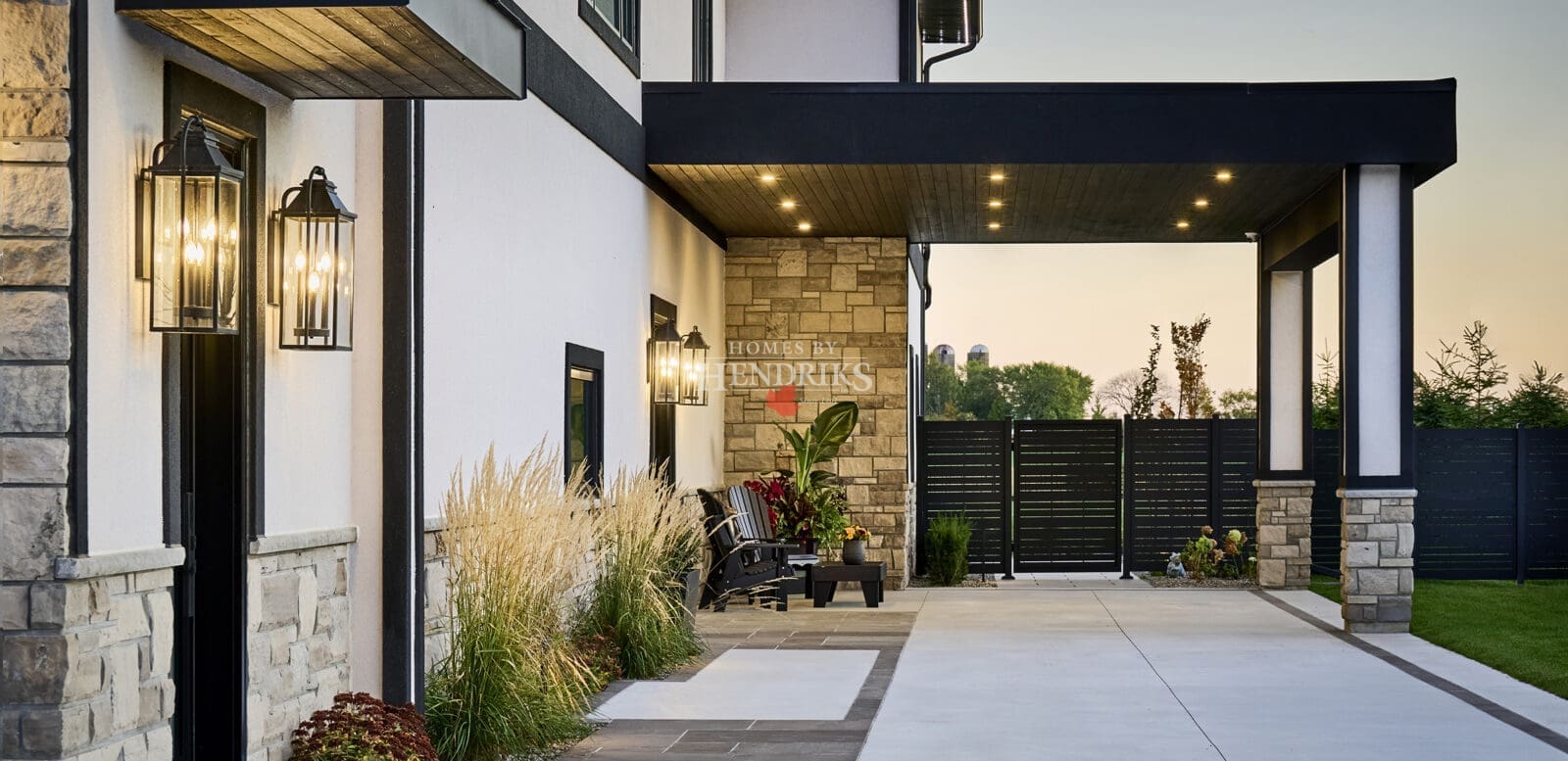 Inviting entry approach framed by stone walls, black accents, and warm outdoor lanterns leading to a covered seating area.