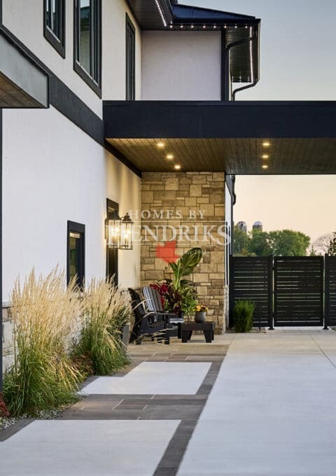 Inviting entry approach framed by stone walls, black accents, and warm outdoor lanterns leading to a covered seating area.