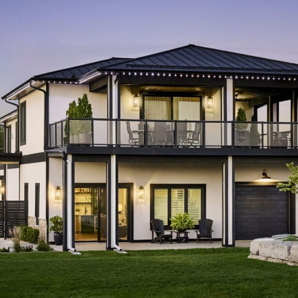 Contemporary two-storey home with white stucco exterior, black trim, glass railings, and upper balcony overlooking manicured landscaping.