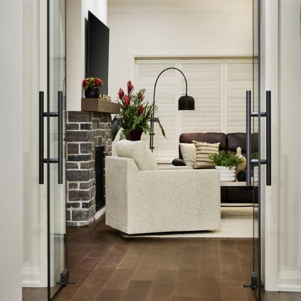 Elegant living room framed by full-height glass doors, featuring a stone fireplace, cozy seating, and layered neutral textures.
