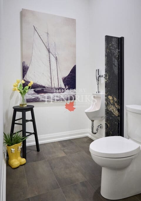 Stylish powder room with wall-mounted urinal, nautical sailboat artwork, black marble accent, and playful yellow rain boot planter.