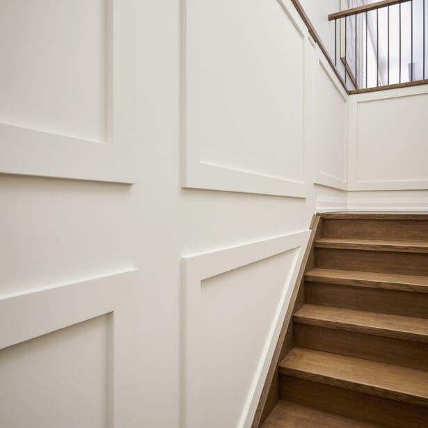 Classic white wainscoting with clean trim lines following a warm oak staircase leading to the upper level.