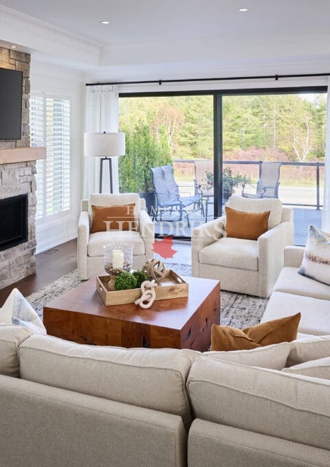 Bright open-concept living room featuring a stone fireplace with wood mantel, sectional seating, and soft neutral décor overlooking an outdoor patio.