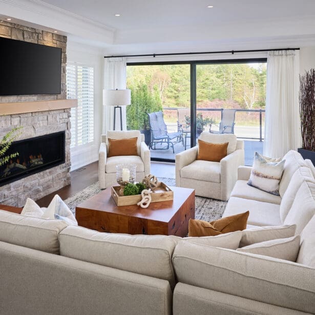 Bright open-concept living room featuring a stone fireplace with wood mantel, sectional seating, and soft neutral décor overlooking an outdoor patio.