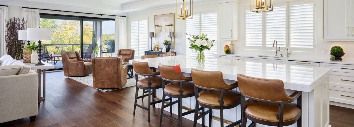 Spacious kitchen and living area with wide-plank hardwood floors, white cabinetry, gold pendant lighting, and caramel leather counter stools.