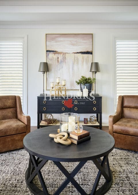 Sophisticated sitting area with leather armchairs, a round black coffee table, and abstract artwork above a navy console accented with brass details.