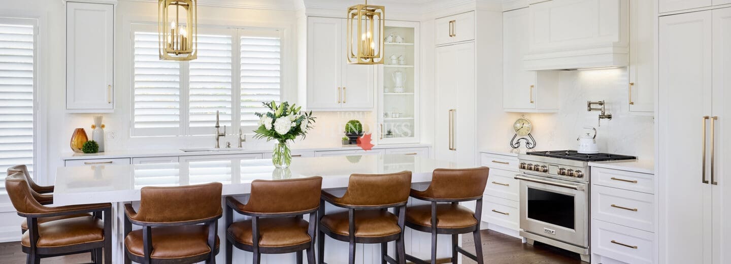 Bright modern kitchen featuring white shaker cabinetry, gold hardware, a large quartz island, and leather counter stools with dark wood frames.