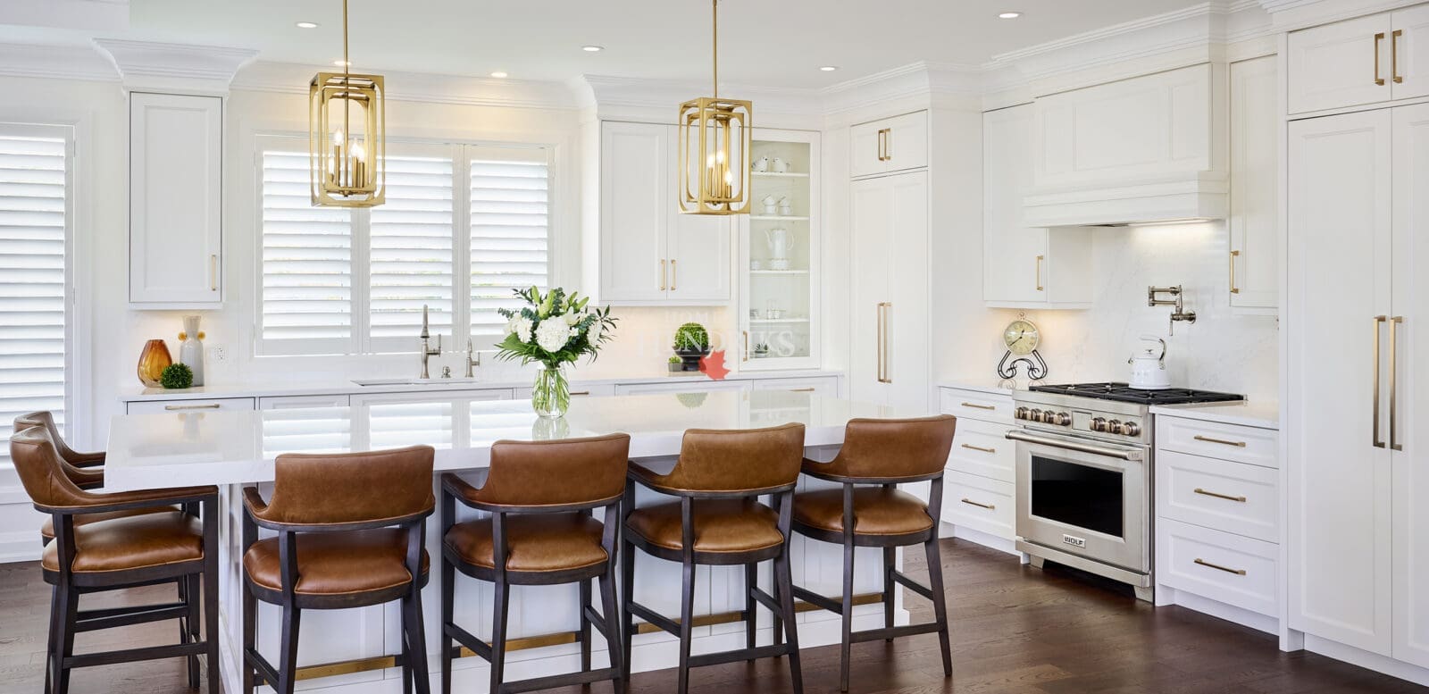 Bright modern kitchen featuring white shaker cabinetry, gold hardware, a large quartz island, and leather counter stools with dark wood frames.