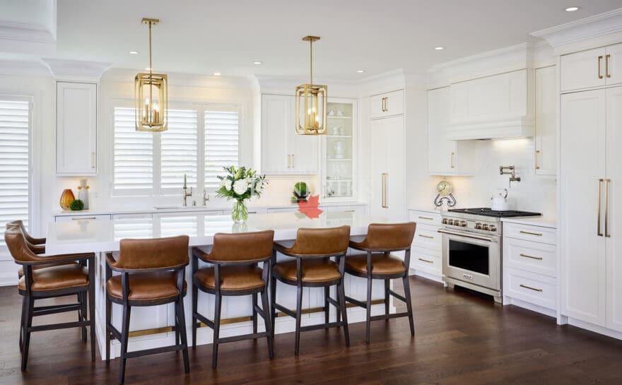 Bright modern kitchen featuring white shaker cabinetry, gold hardware, a large quartz island, and leather counter stools with dark wood frames.