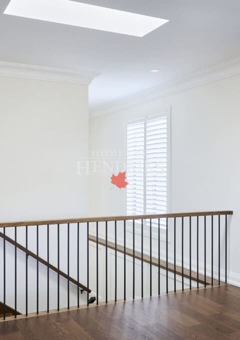 Open upper hallway with oak flooring, white walls, black railing, and oversized abstract artwork beneath a skylight.