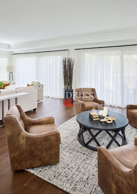 Bright great room with stone fireplace, neutral sectional sofa, and leather armchairs creating a cozy, refined gathering area.