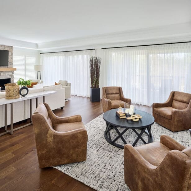 Bright great room with stone fireplace, neutral sectional sofa, and leather armchairs creating a cozy, refined gathering area.