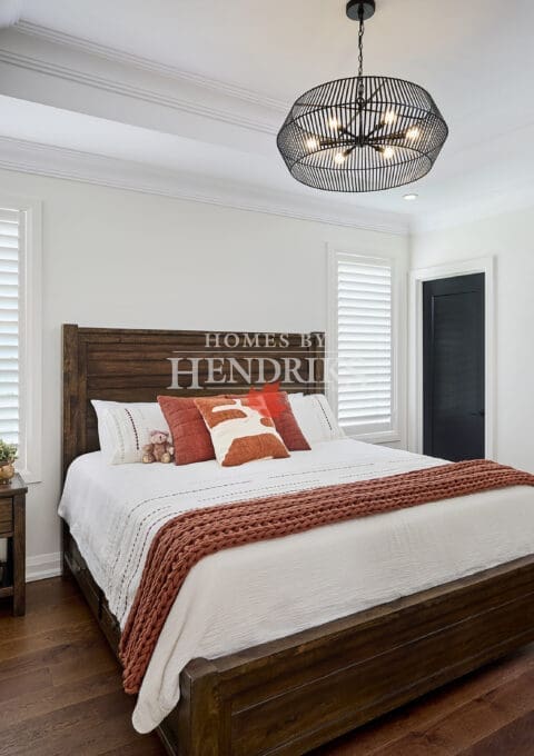 Warm and inviting bedroom with dark wood furniture, layered textiles in rust and ivory tones, and a modern black cage chandelier.