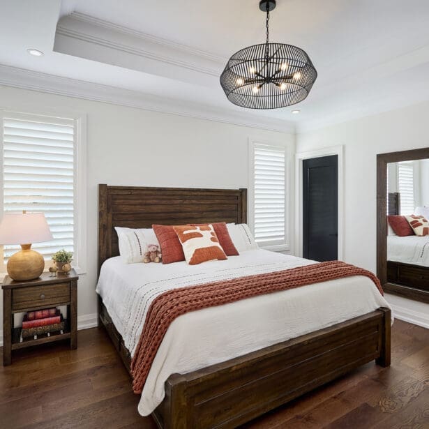 Warm and inviting bedroom with dark wood furniture, layered textiles in rust and ivory tones, and a modern black cage chandelier.