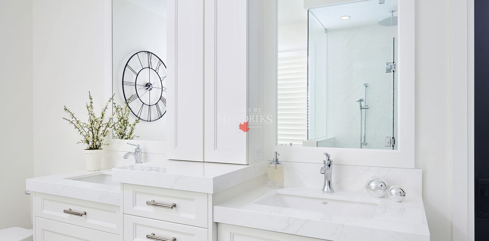 Elegant white double vanity with marble countertops, chrome hardware, and framed mirrors under soft recessed lighting.