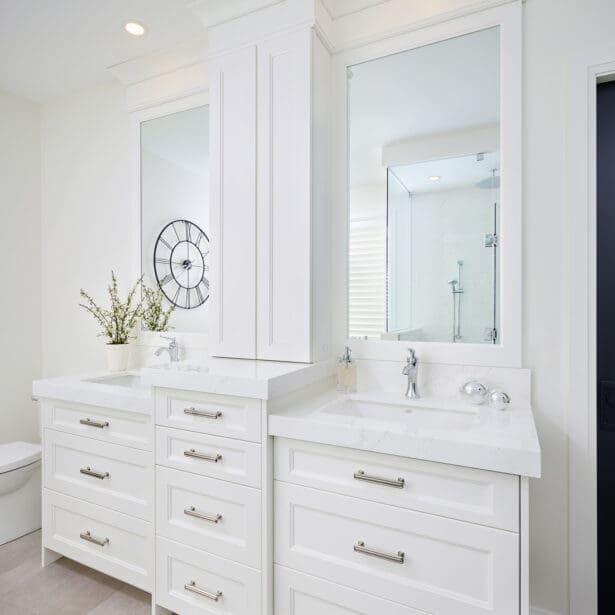 Elegant white double vanity with marble countertops, chrome hardware, and framed mirrors under soft recessed lighting.