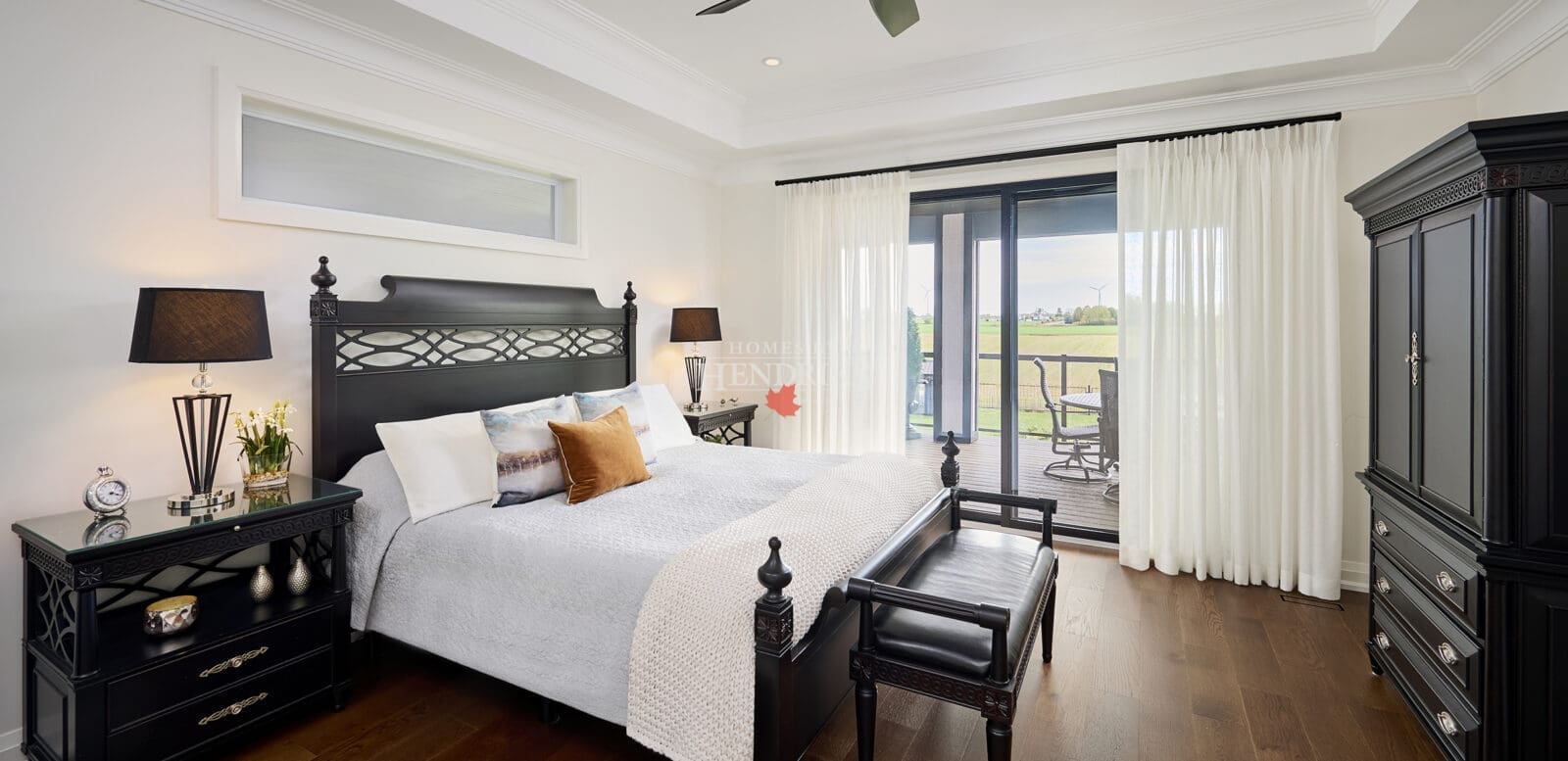 Sophisticated bedroom with black carved wood furniture, soft neutral bedding, and sliding glass doors opening to a private terrace with countryside views.