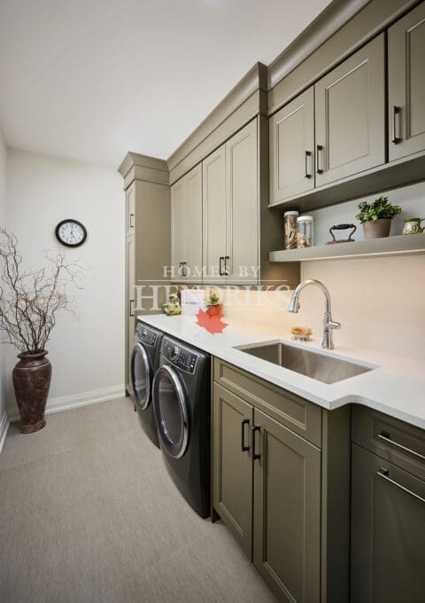 Functional yet stylish laundry space with sage cabinetry, black hardware, quartz countertops, and front-load washer and dryer.
