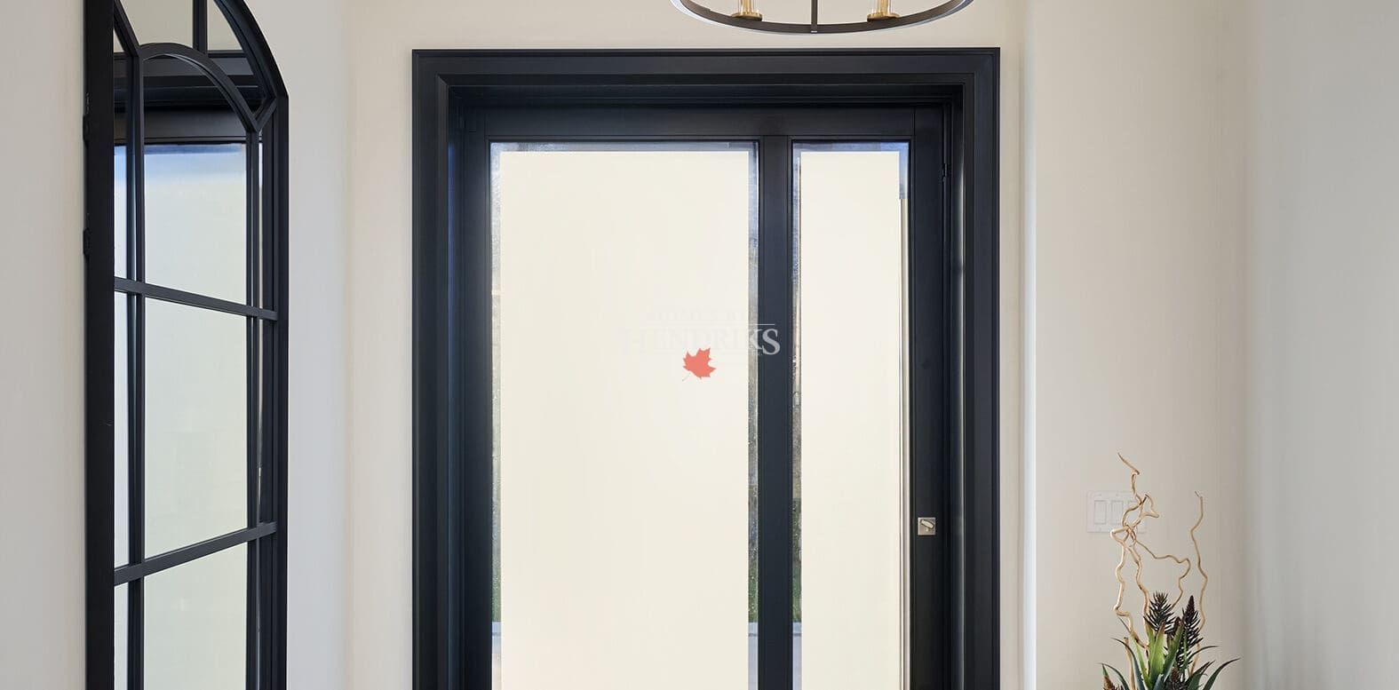 Front Foyer Bright entryway with black-framed glass doors, two-tier chandelier, large arched mirror, and warm wood flooring.