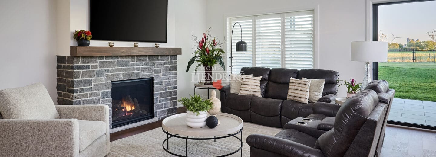 Cozy family room with stone fireplace, dark leather seating, and expansive sliding doors overlooking the backyard.