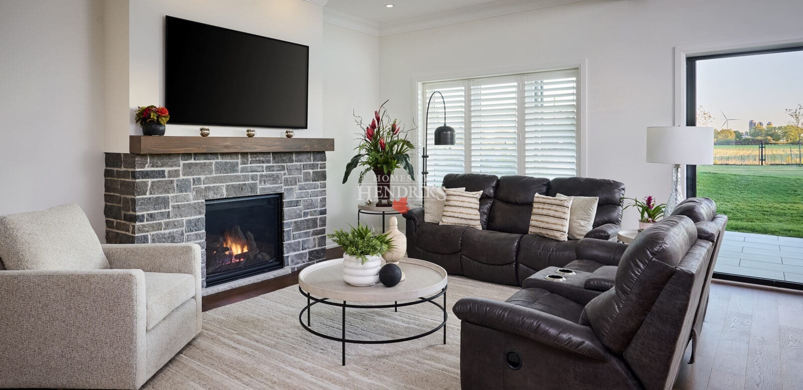 Cozy family room with stone fireplace, dark leather seating, and expansive sliding doors overlooking the backyard.