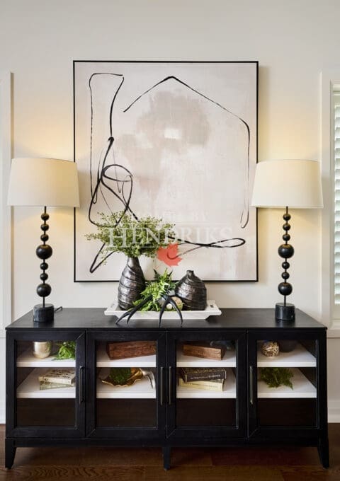 Decorative console vignette with matte black cabinet, abstract wall art, sculptural table lamps, and layered organic accents.