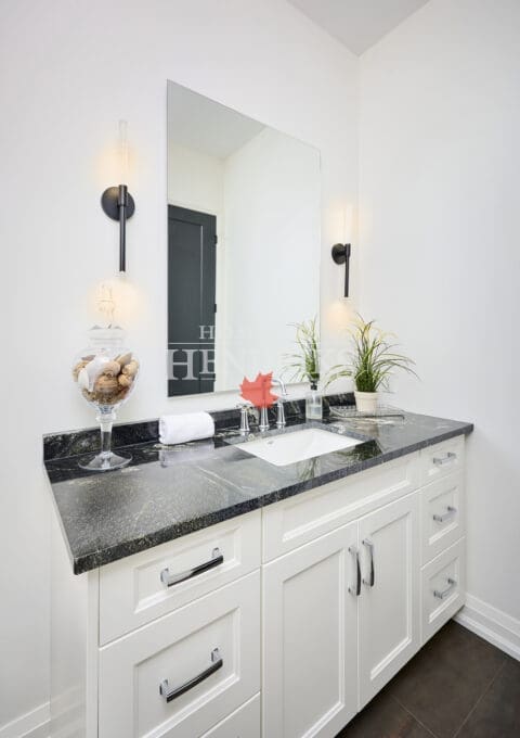 Bright white vanity with black stone countertop, wall-mounted sconces, and chrome fixtures creating a clean and timeless bathroom design.