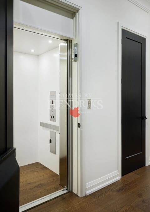Sleek residential elevator with stainless steel trim, recessed lighting, and adjacent black interior door for a seamless modern aesthetic.