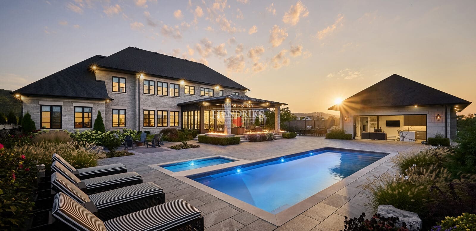 Stunning custom home with a luxurious stone exterior featuring limestone accents, surrounded by lush landscaping and a beautifully designed pool, showcasing an elegant and timeless architectural style.