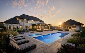 Stunning custom home with a luxurious stone exterior featuring limestone accents, surrounded by lush landscaping and a beautifully designed pool, showcasing an elegant and timeless architectural style.