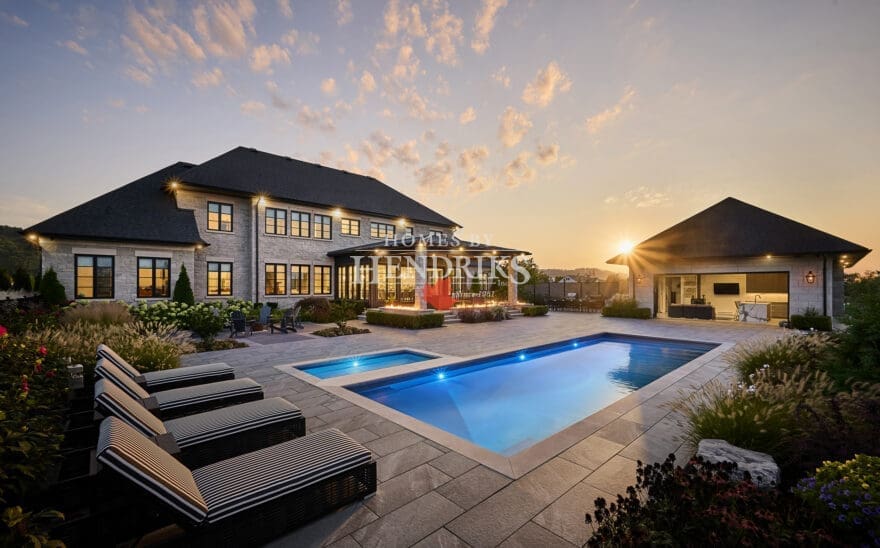 Stunning custom home with a luxurious stone exterior featuring limestone accents, surrounded by lush landscaping and a beautifully designed pool, showcasing an elegant and timeless architectural style.
