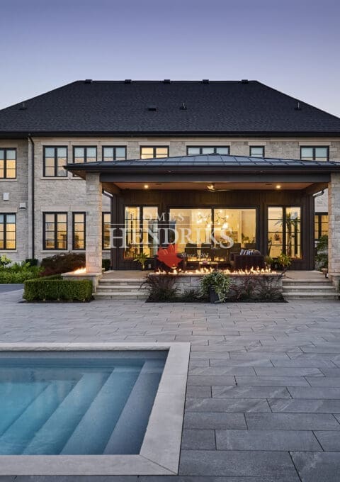 Elegant custom home with a beautiful stone exterior, limestone accents, and a stunning pool area surrounded by lush landscaping.