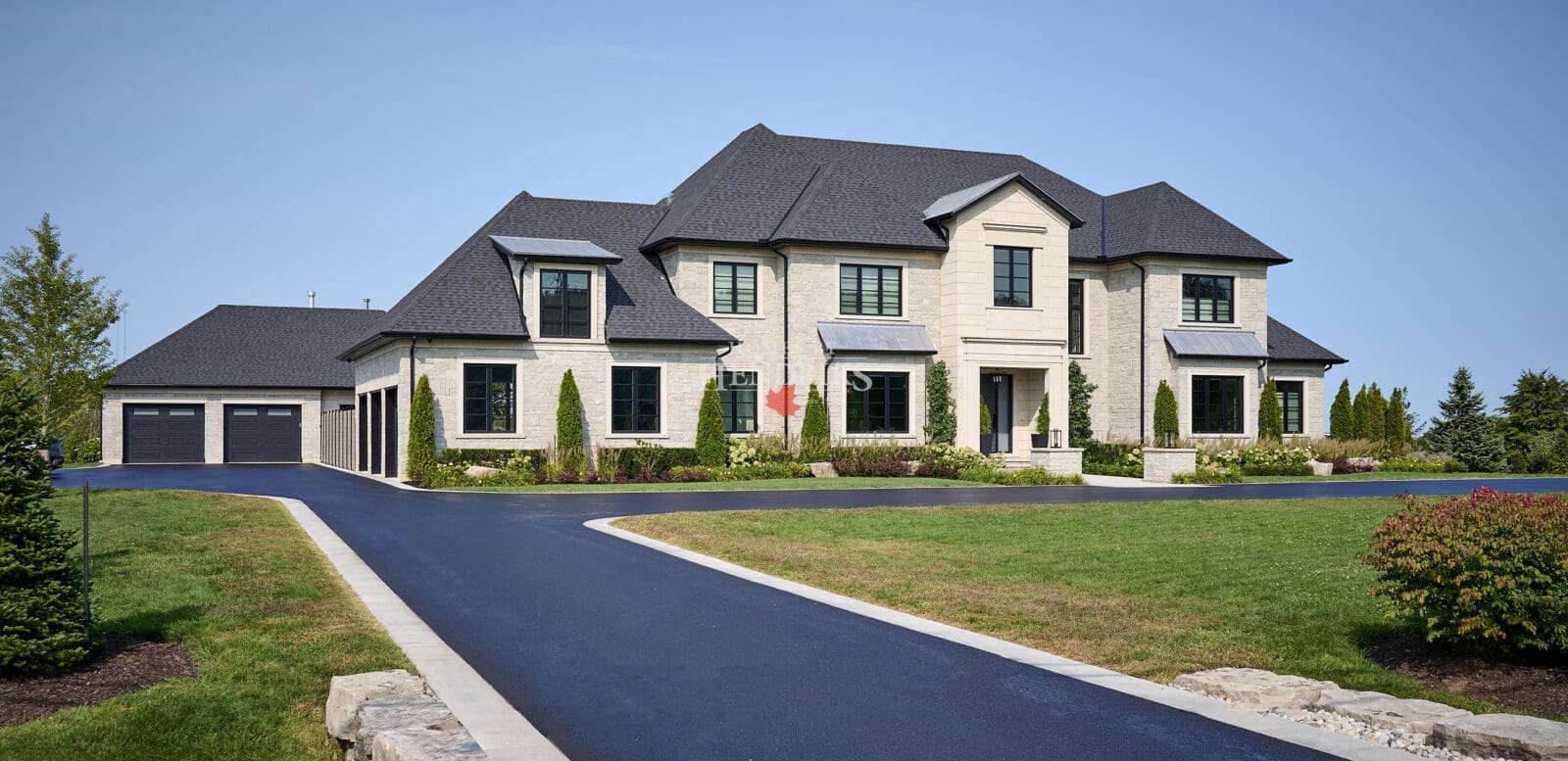 Front entry way on a custom home featuring limestone accents, paved driveway and a beautiful landscape. Chateau Style Home
