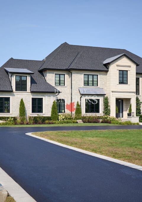Front entry way on a custom home featuring limestone accents, paved driveway and a beautiful landscape. Chateau Style Home