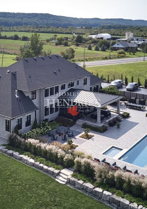 Refined custom home with a rich stone exterior and limestone detailing, complemented by a lush garden and sparkling pool.