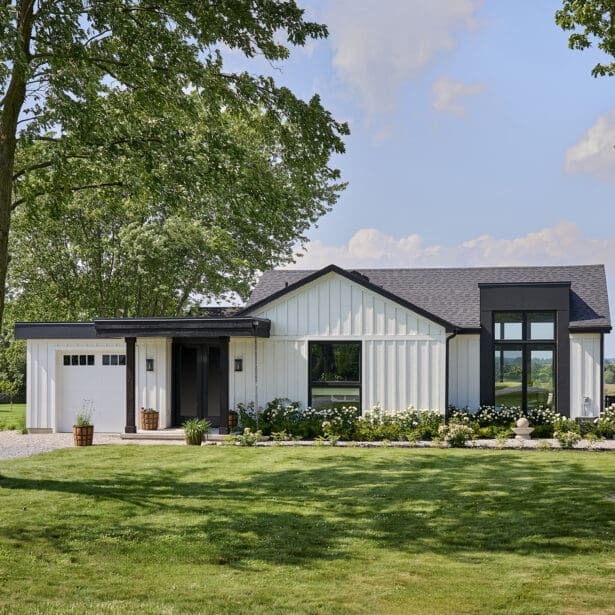 Modern farmhouse exterior featuring white vertical siding, black-framed windows, covered porch, and stone landscaping.