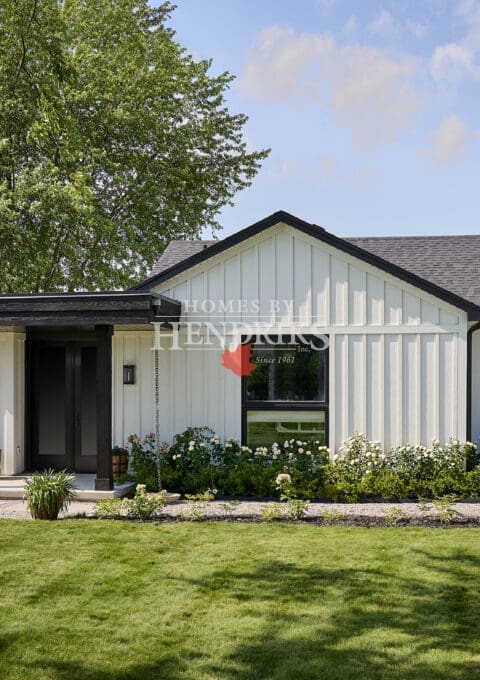Close-up of covered front entrance with wood posts, black front door, stone steps, and decorative planters.