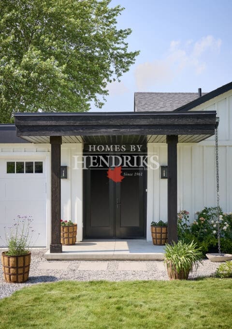 Front corner view of custom modern farmhouse with attached garage, black entry canopy, and landscaped gardens.
