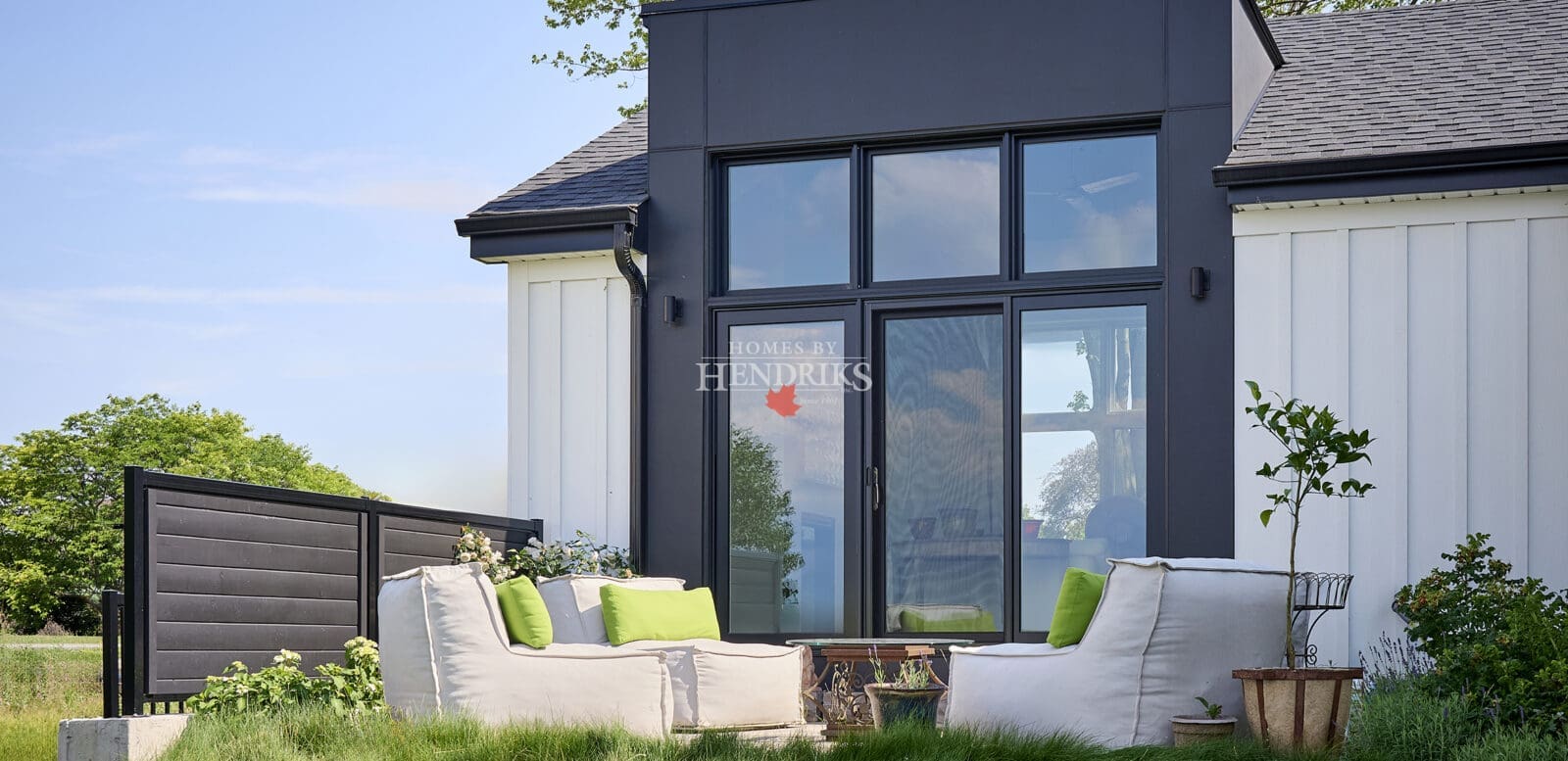 Close-up of contemporary rear elevation featuring floor-to-ceiling windows and outdoor patio overlooking the lawn.