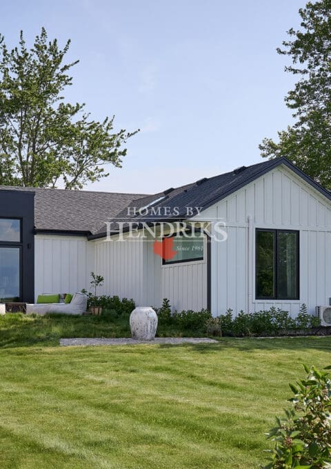 Rear view of modern custom bungalow with expansive lawn, black window feature, and covered outdoor living area.