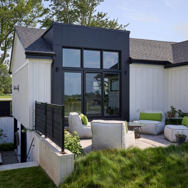 Modern backyard patio with black-framed windows, outdoor lounge furniture, and raised landscaping.