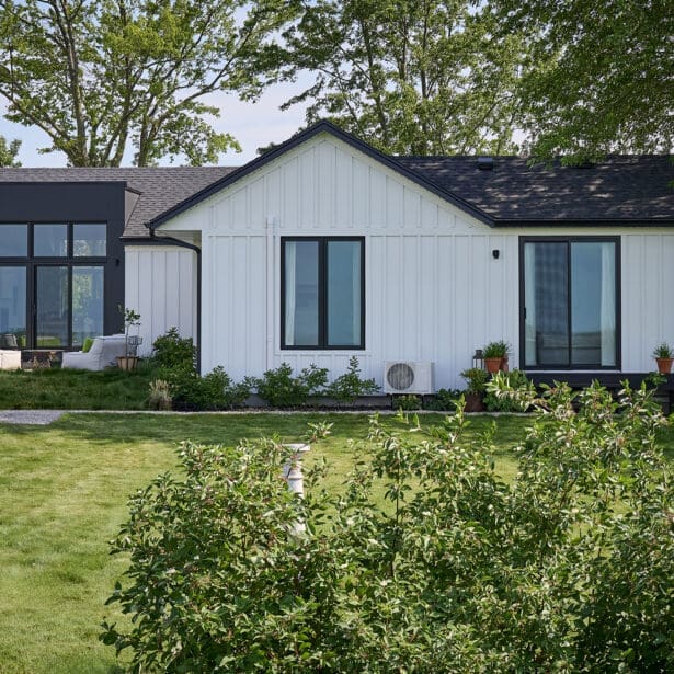 Rear elevation of white board-and-batten custom home with black trim, large windows, and spacious backyard.